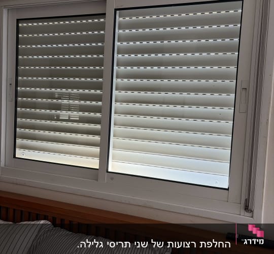 חלון עם תריסים סגורים מעל מיטה